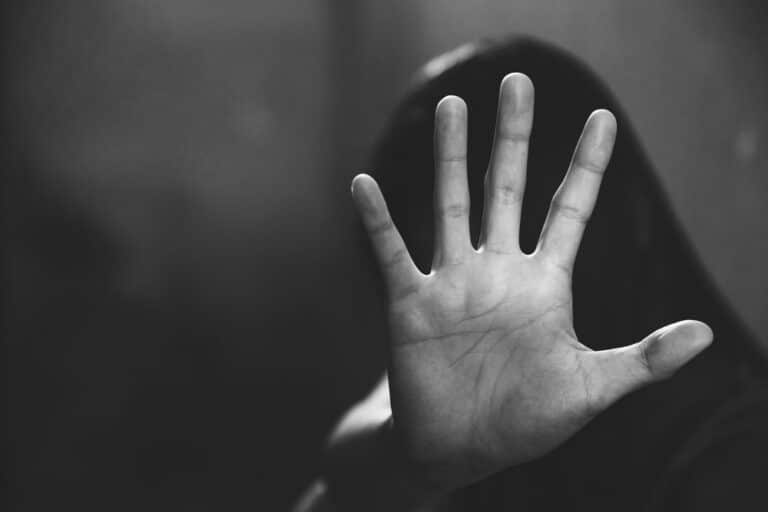 Image is of a raised hand signaling stop in front of a blurred figure, concept of sexual assault in Washington and personal safety awareness.