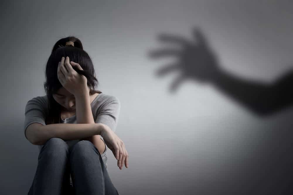 Image is of a distressed survivor sitting alone with a shadow reaching toward her, concept of sexual assault in Washington and seeking legal protection.
