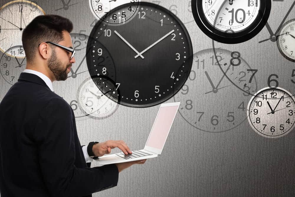 Image is of a professional working on a laptop surrounded by multiple clocks, representing workplace time compliance and labor law protections for employees.