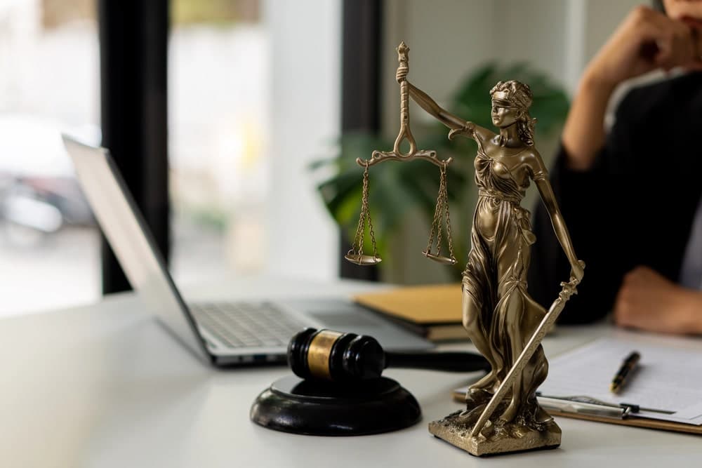Image is of Lady Justice statue on an office desk with legal documents, concept of labor law fairness and employee protections.