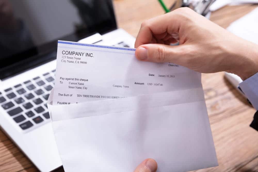 Image is of a person opening a paycheck envelope near a laptop, concept of labor law wage protection and payroll rights.