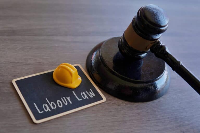 Image is of a judge gavel beside a labor law sign and safety helmet, concept of labor law protections for workplace rights.