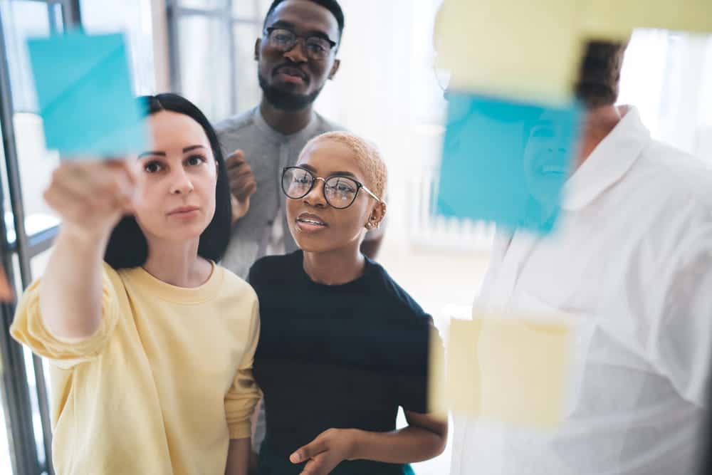 Image is of diverse coworkers reviewing notes on glass wall during a planning session, highlighting how union workers collaborate to protect shared employment rights.