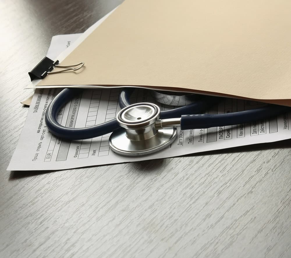 Image is of medical records and a stethoscope on a desk, highlighting injury documentation needed for a mass tort lawsuit.