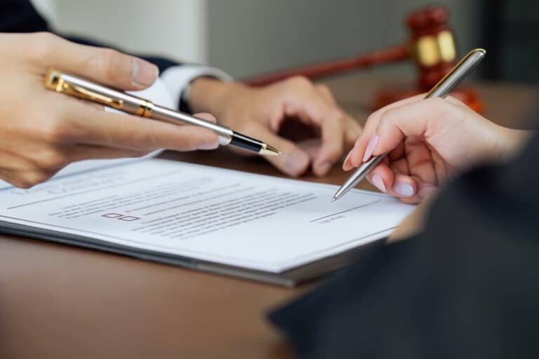 Image is of two individuals reviewing and signing legal documents together, concept of mass tort claims consultation