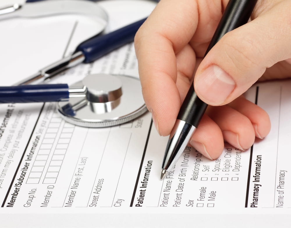 Image is of a person filling out a medical form with a stethoscope nearby, concept of eligibility for mass tort claims