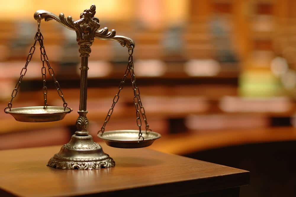 Image is of a courtroom scale of justice placed on a wooden table, representing balance and legal process timelines for lawsuits in Cincinnati