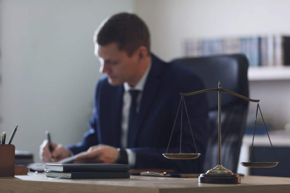 Image is of a lawyer reviewing documents at a desk with scales of justice, reflecting legal processes in litigation in Kentucky