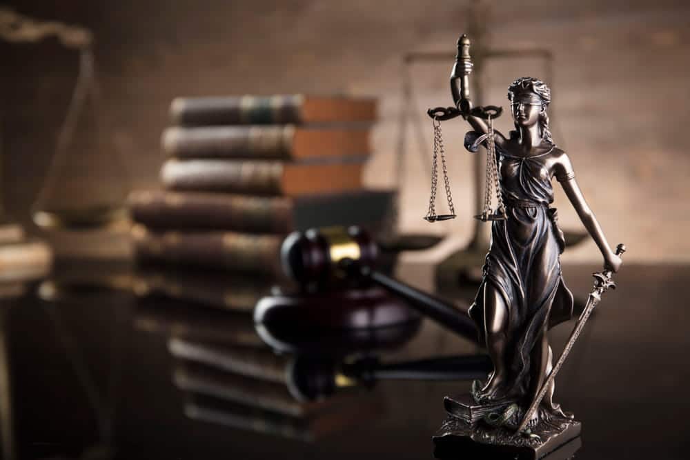 Image is of a Lady Justice statue with scales and a gavel on a desk, representing civil litigation and legal decision making