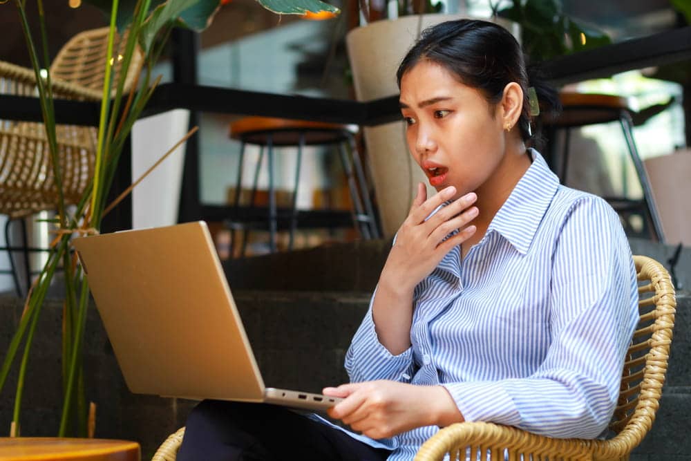 Image is of a woman reacting with shock while viewing content online, concept of harm caused by AI-Generated images