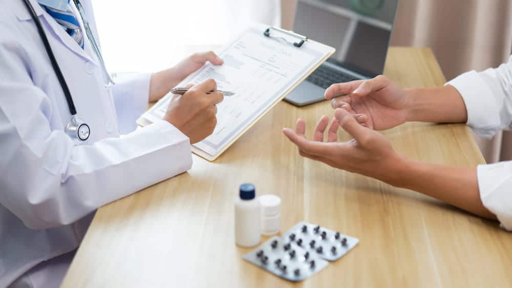 Image is of a doctor consulting a patient and reviewing treatment notes, discussing breast mesh concerns and possible complications