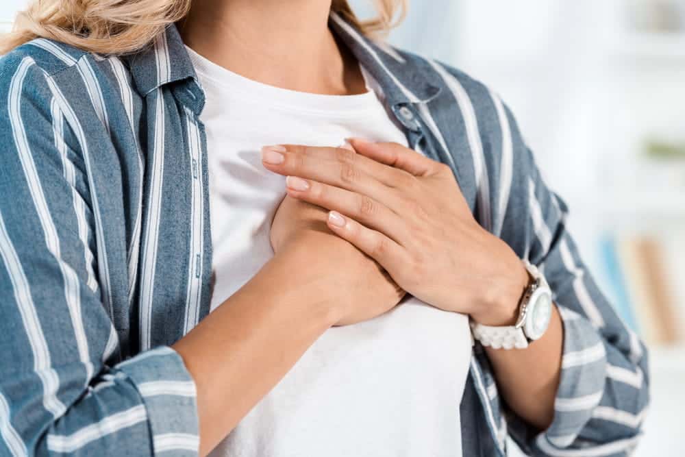 Image is of a woman placing her hand over her chest, representing early signs of breast mesh failure such as soreness and internal discomfort