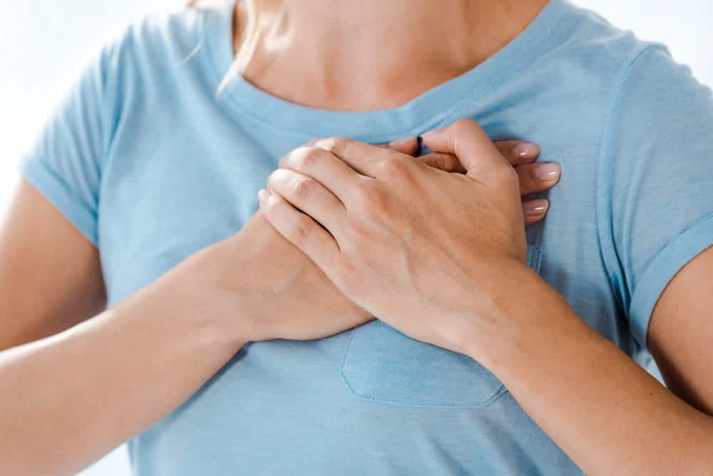 Image is of a woman holding her chest in discomfort, showing pain and tenderness linked to breast mesh failure after surgery