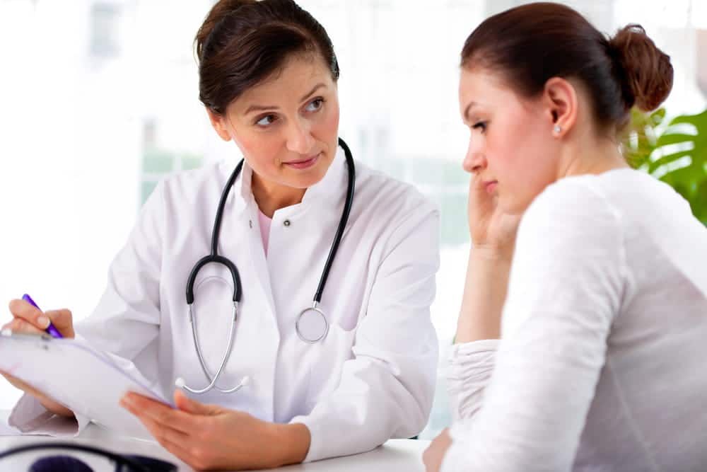 Image is of a doctor consulting with a patient during a medical visit, discussing symptoms related to breast mesh complication