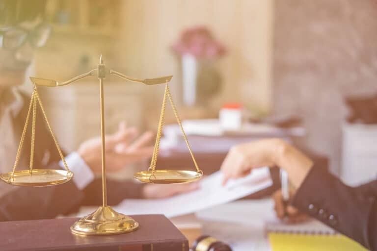 Image is of a balance scale on a lawyer’s desk, concept of legal action in AI image abuse cases