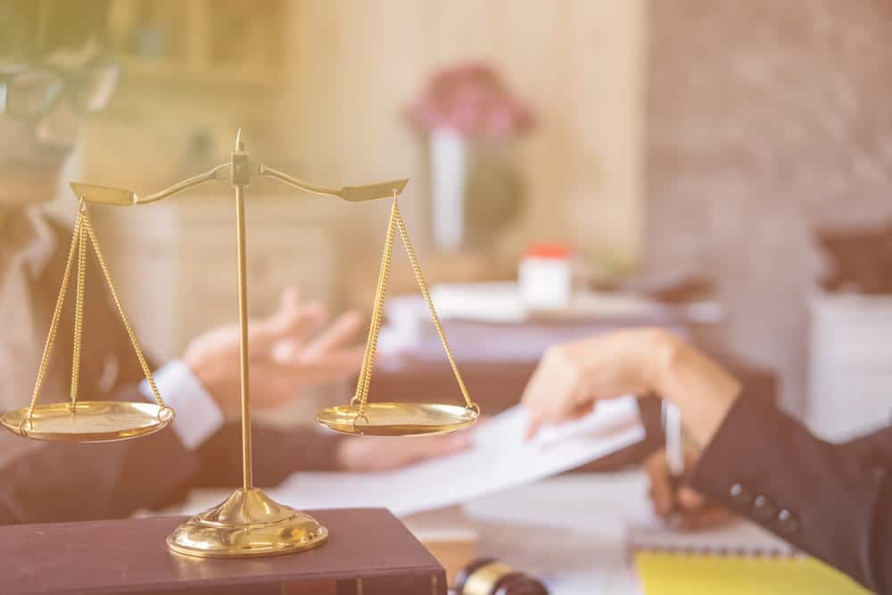 Image is of a balance scale on a lawyer’s desk, concept of legal action in AI image abuse cases