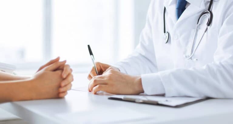 Image is of a doctor consulting with a patient during a medical appointment, discussing complications related to breast mesh