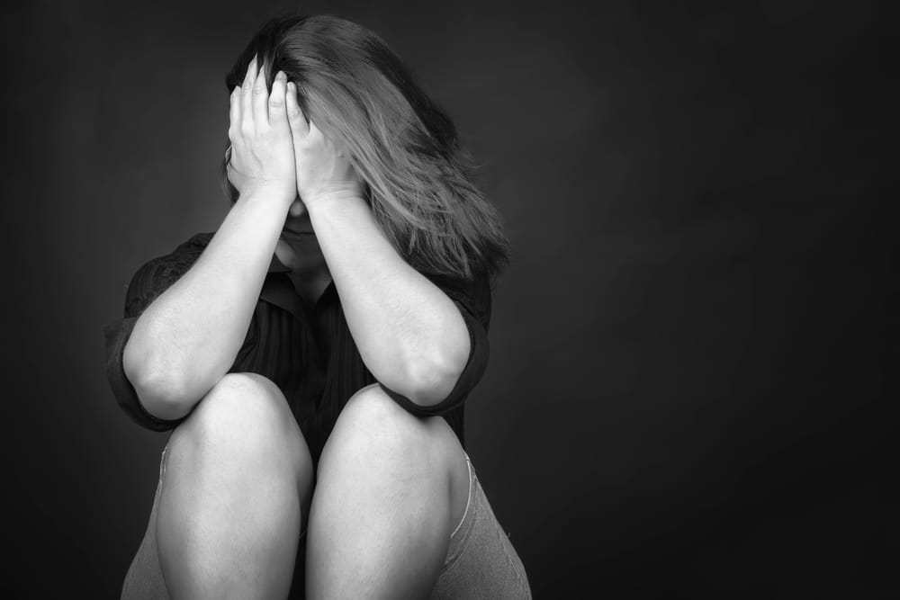 Image is of a woman sitting with her face covered in distress, representing the emotional impact of sexual assault in Nashville