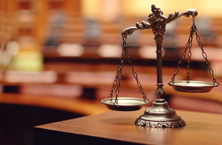 Image is of balanced scales in a courtroom setting, symbolizing the legal process and justice after sexual assault in Nashville