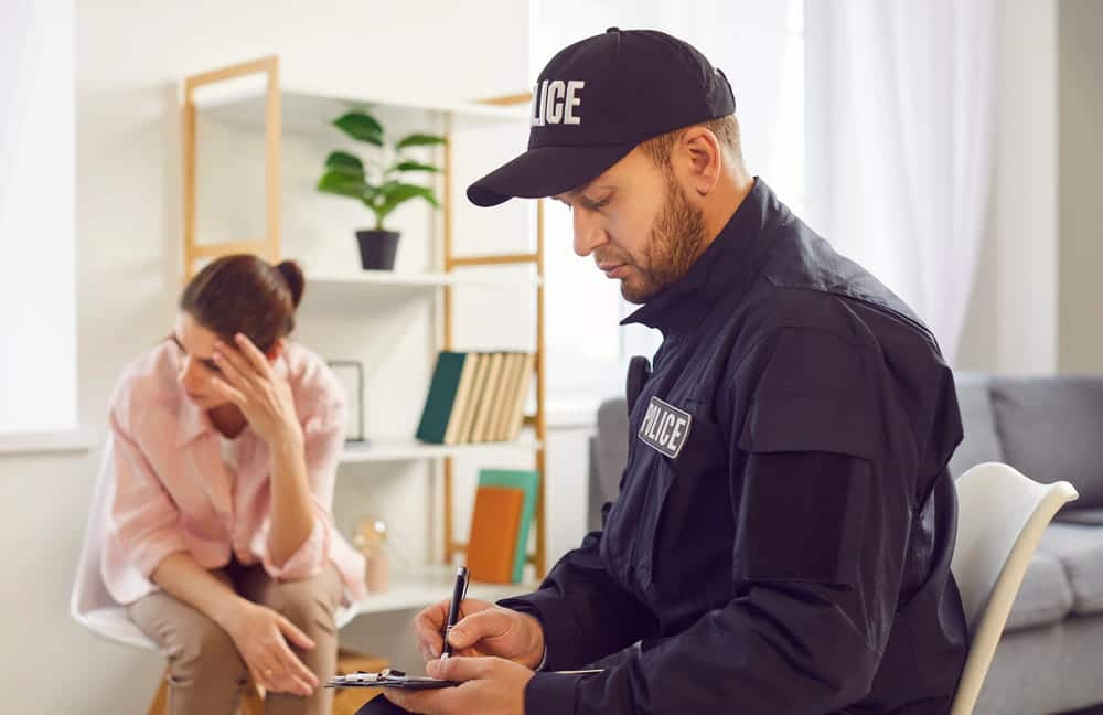 Image is of a police officer taking notes while speaking with a distressed woman at home, showing reporting process after sexual assault in Nashville