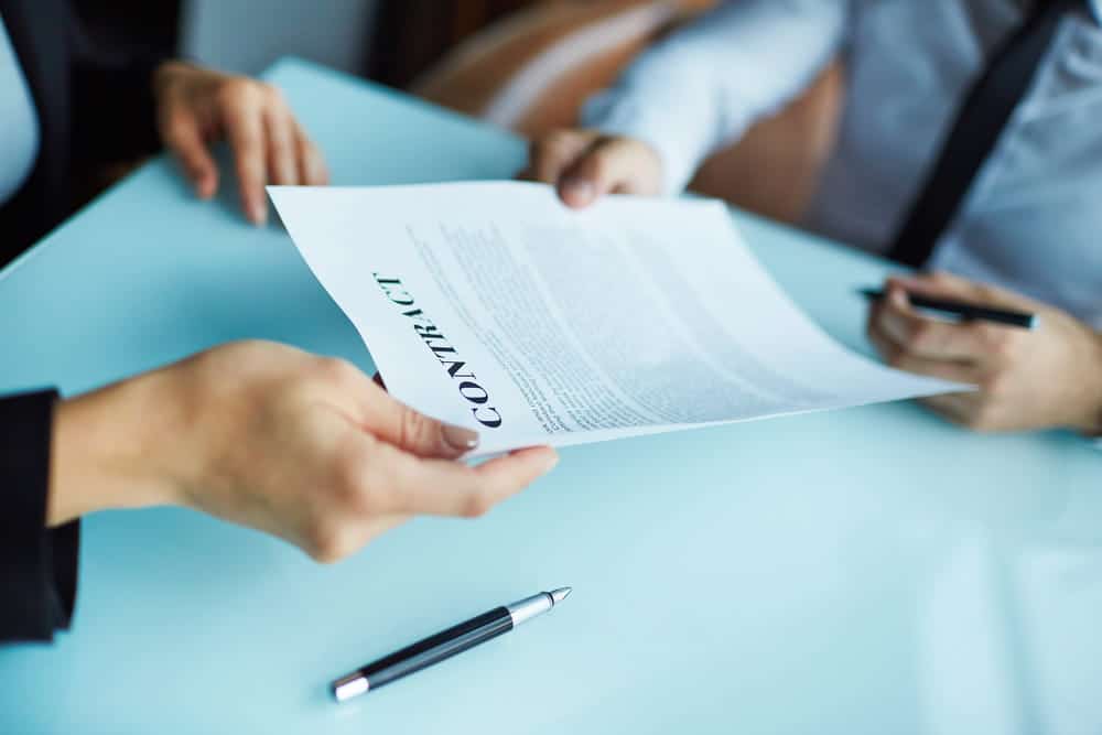 Image is of individuals exchanging and reviewing an employment agreement document, concept of labor contract enforcement and workplace obligations in Ohio.