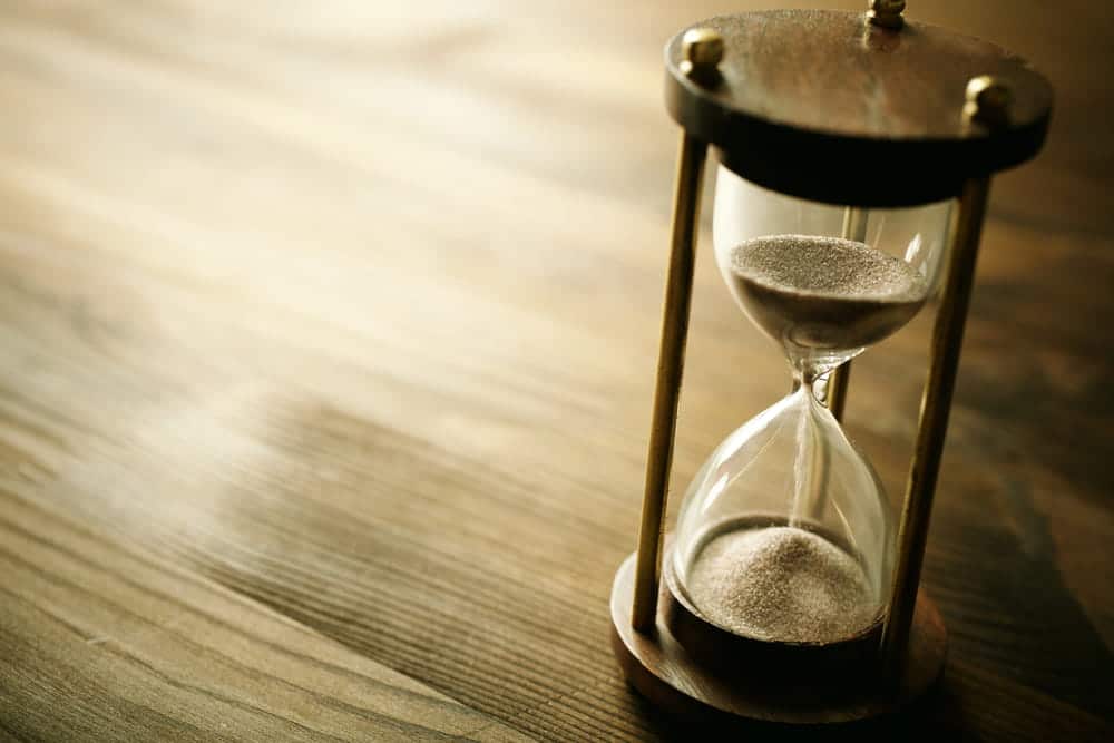 Image is of a close-up hourglass with sand flowing on a wooden table, concept of timelines in mass tort cases
