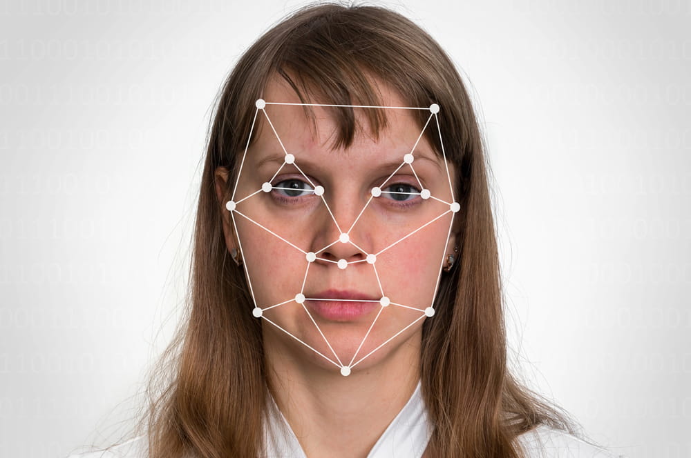 Image is of a person with facial mapping technology displayed across the face, concept of AI harassment involving biometric data, facial recognition systems, and potential privacy concerns.