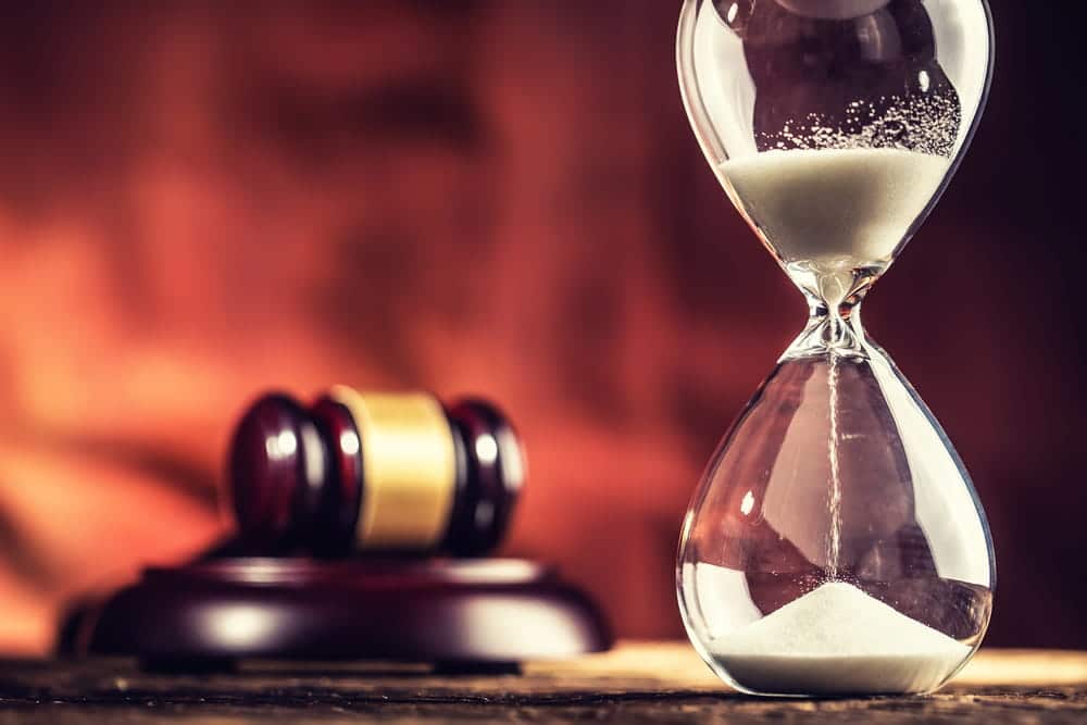 Image is of a courtroom gavel beside an hourglass, concept of the time involved in a lawsuit and the legal process in Louisville.