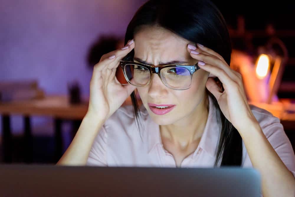 Image is of a woman looking concerned while using a laptop, concept of deepfake images causing privacy, reputation, and online safety concerns.