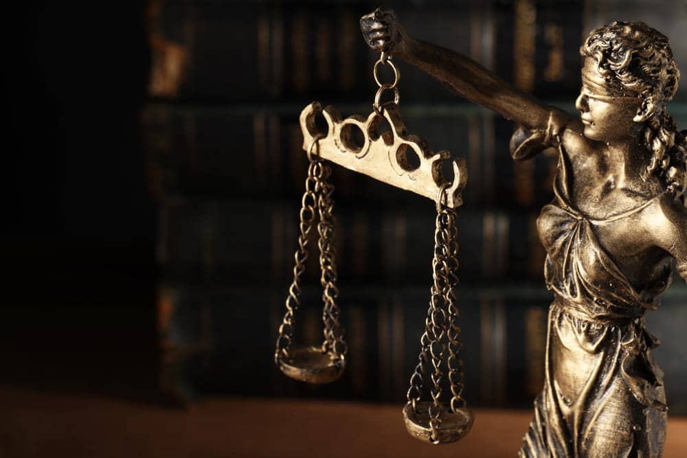 Image is of Lady Justice holding scales, representing the legal process leading to a trial in Louisville.