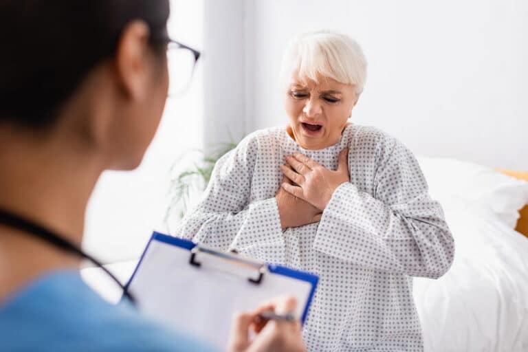 Image is of a patient experiencing chest pain while speaking with a medical professional, concept of breast mesh failure symptoms.