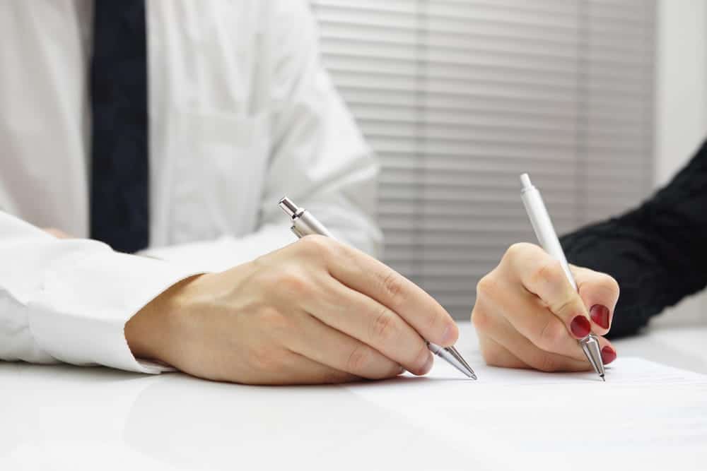 Image is of two people signing legal documents, concept of settlement negotiation and written settlement terms.