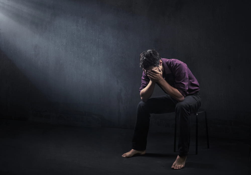 Image is of a distressed person sitting alone with his face covered, representing emotional harm documented in a sexual assault lawsuit.