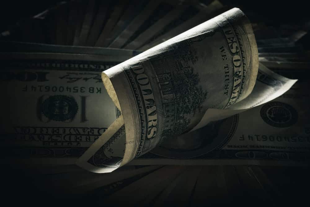 Image of rolled hundred-dollar bills surrounded by US currency, representing potential financial compensation and damages available to plaintiffs in KY mass torts cases.