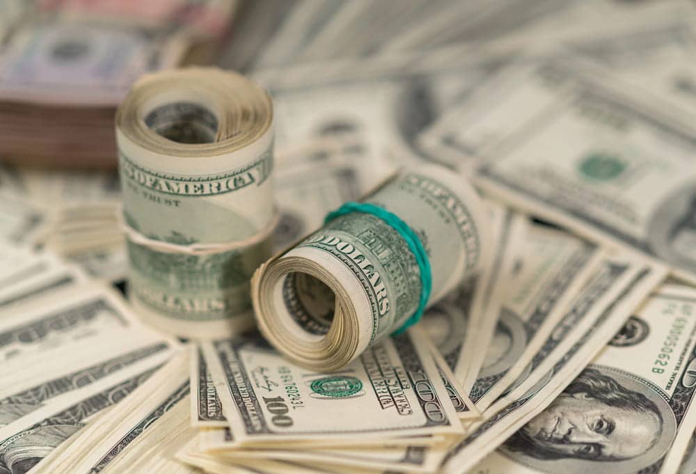 Image is of rolled American dollar bills surrounded by cash, representing potential financial compensation available in Ohio mass torts.